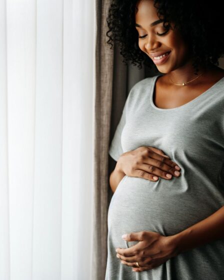 Eine glückliche schwangere Frau in grauem Kleid hält ihre Hände auf ihren Bauch. Was gilt rechtlich für Elternzeit? Ein Anwalt für Arbeitsrecht gibt Antworten.