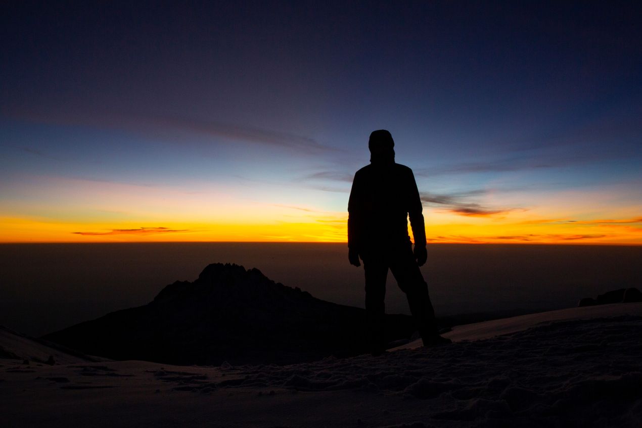 Silhouette eines Bergsteigers bei Sonnenaufgang auf dem Gipfel, ein magischer Moment der Besteigung des Kilimandscharo