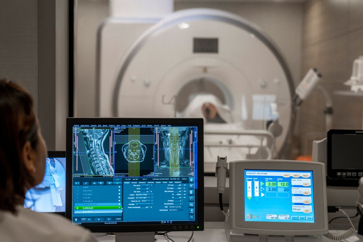 Eine Fachkraft analysiert MRT-Bilder auf einem Bildschirm, während im Hintergrund ein Patient untersucht wird. Fortschrittliche Diagnostik in der Radiologie Dortmund.